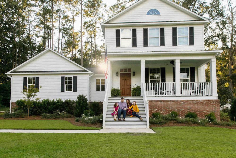 Family standing outside front of new construction white siding farmhouse in the suburbs